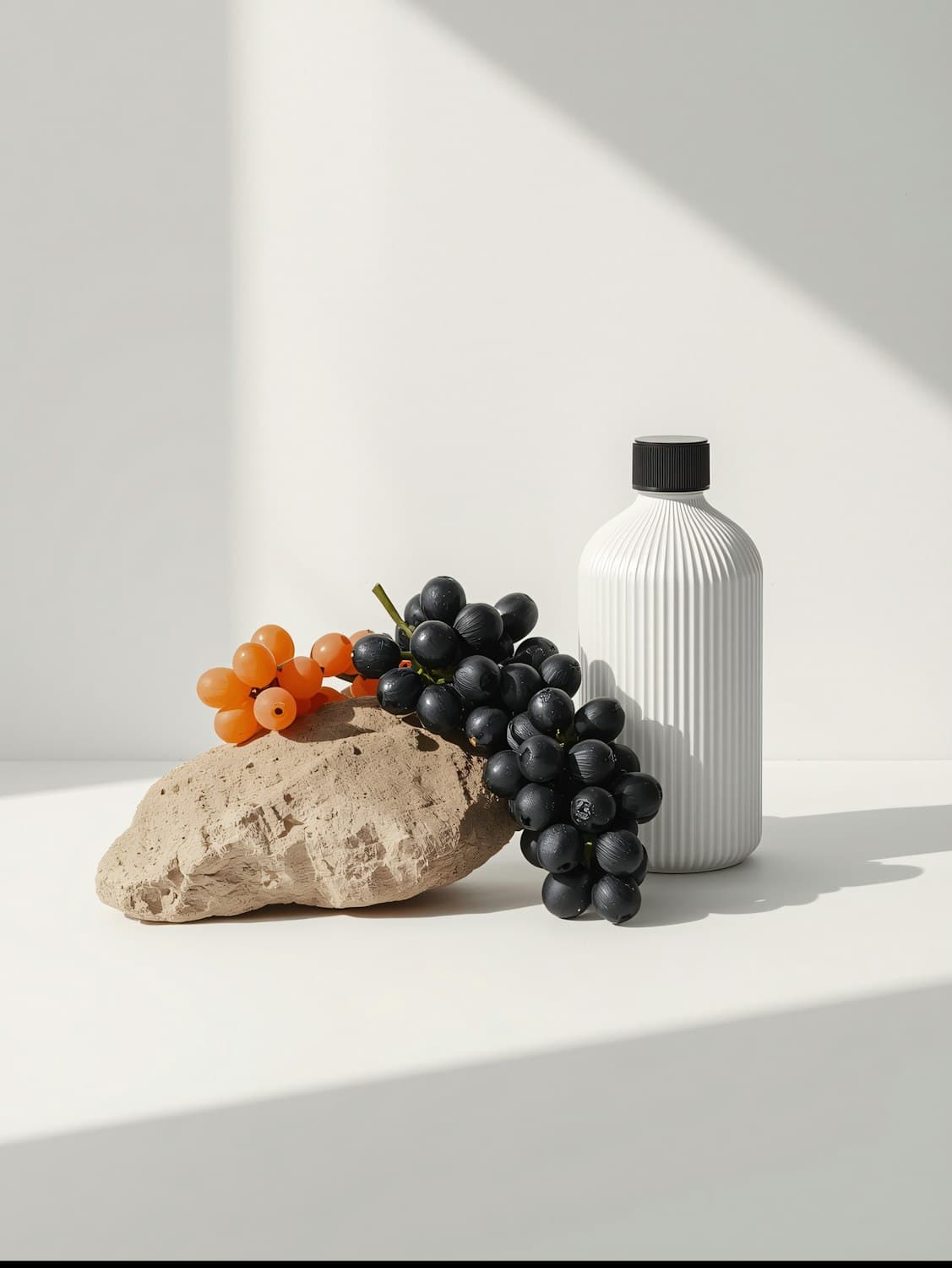 A ribbed white bottle beside grapes and a textured rock